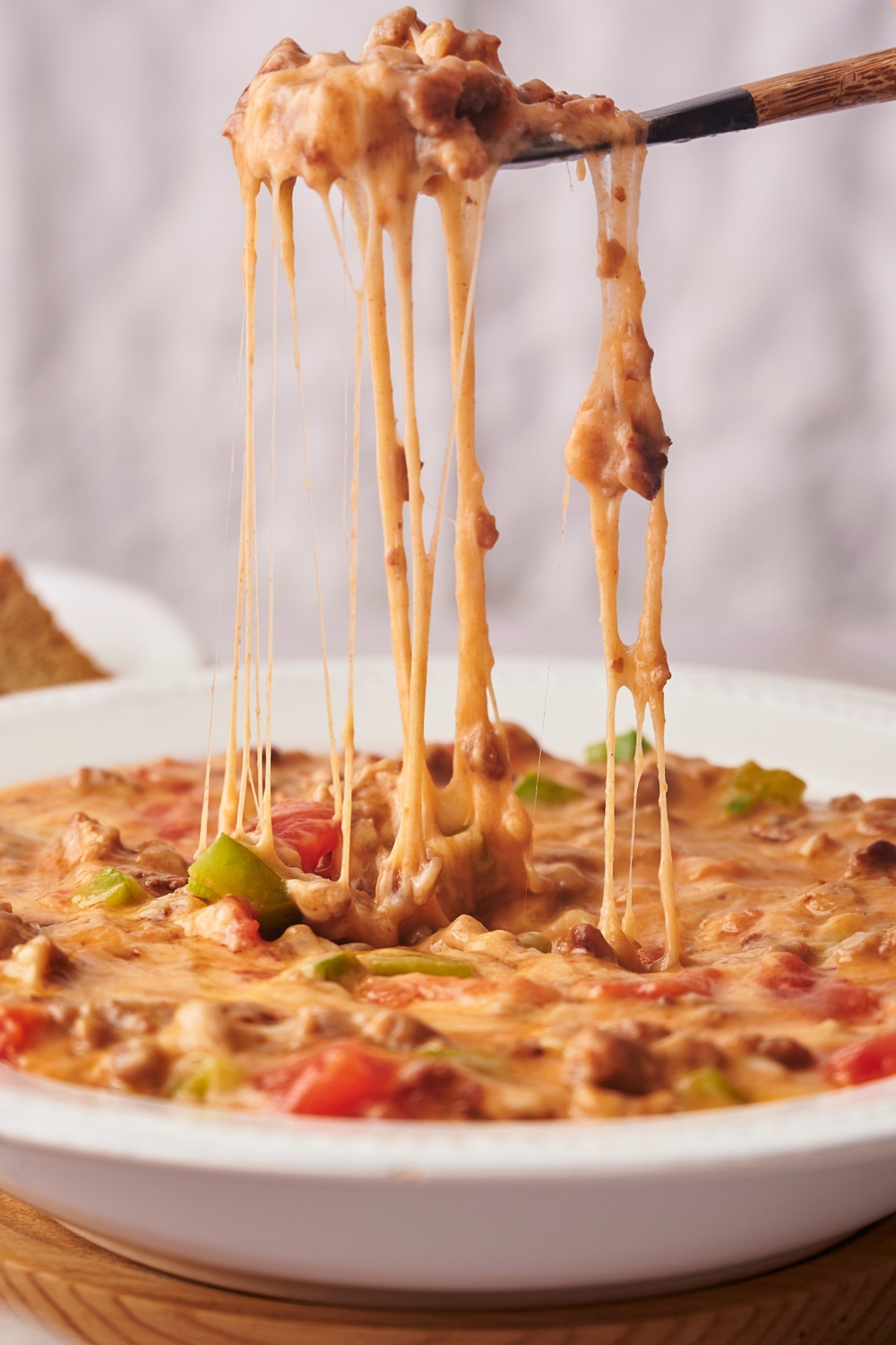 A spoon with rotel dip on in strining down into a bowl filled with the dip.