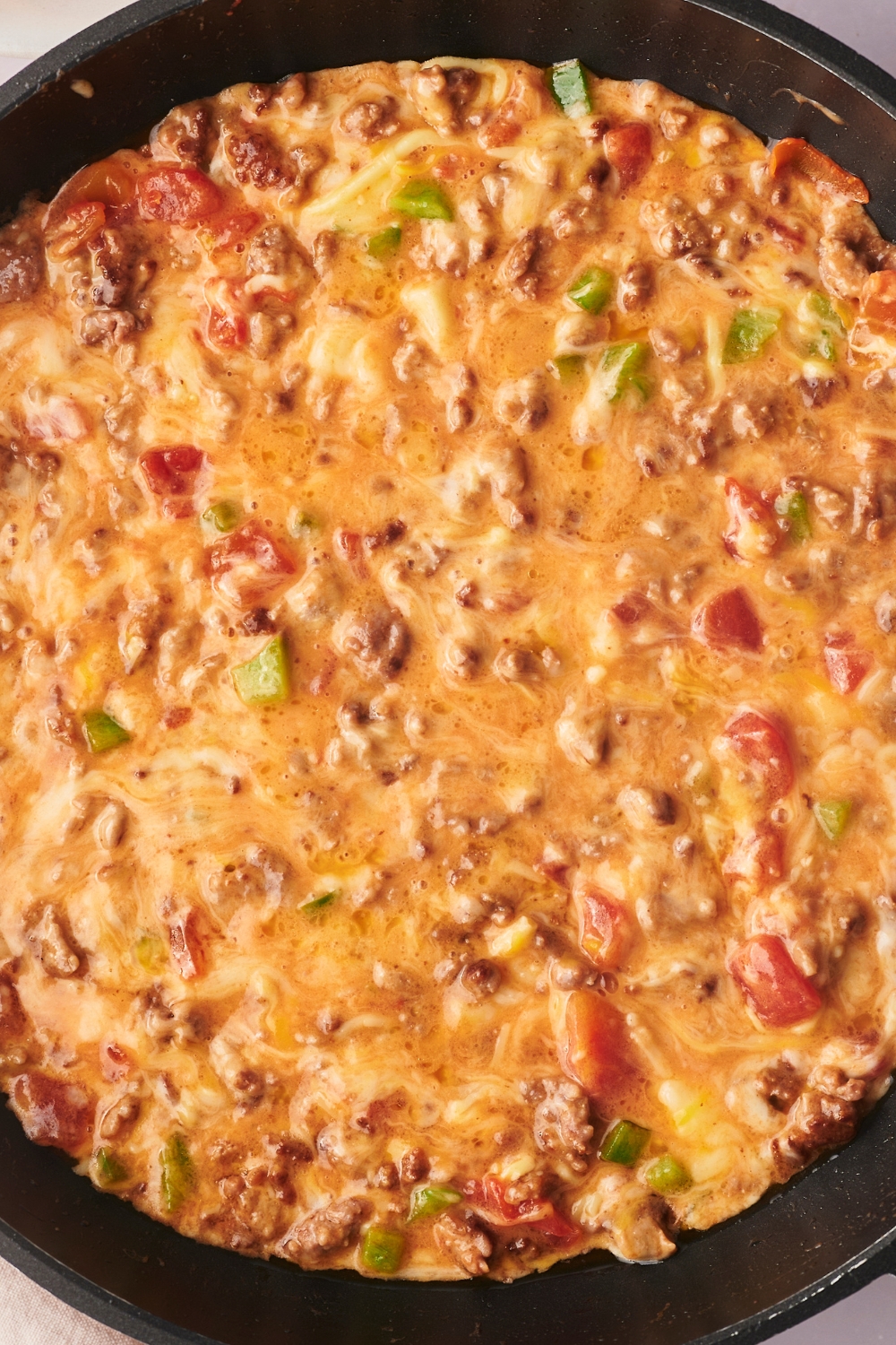 Part of a skillet with melted cheese, Rotel tomatoes, green chiles, and ground sausage all combined in it.