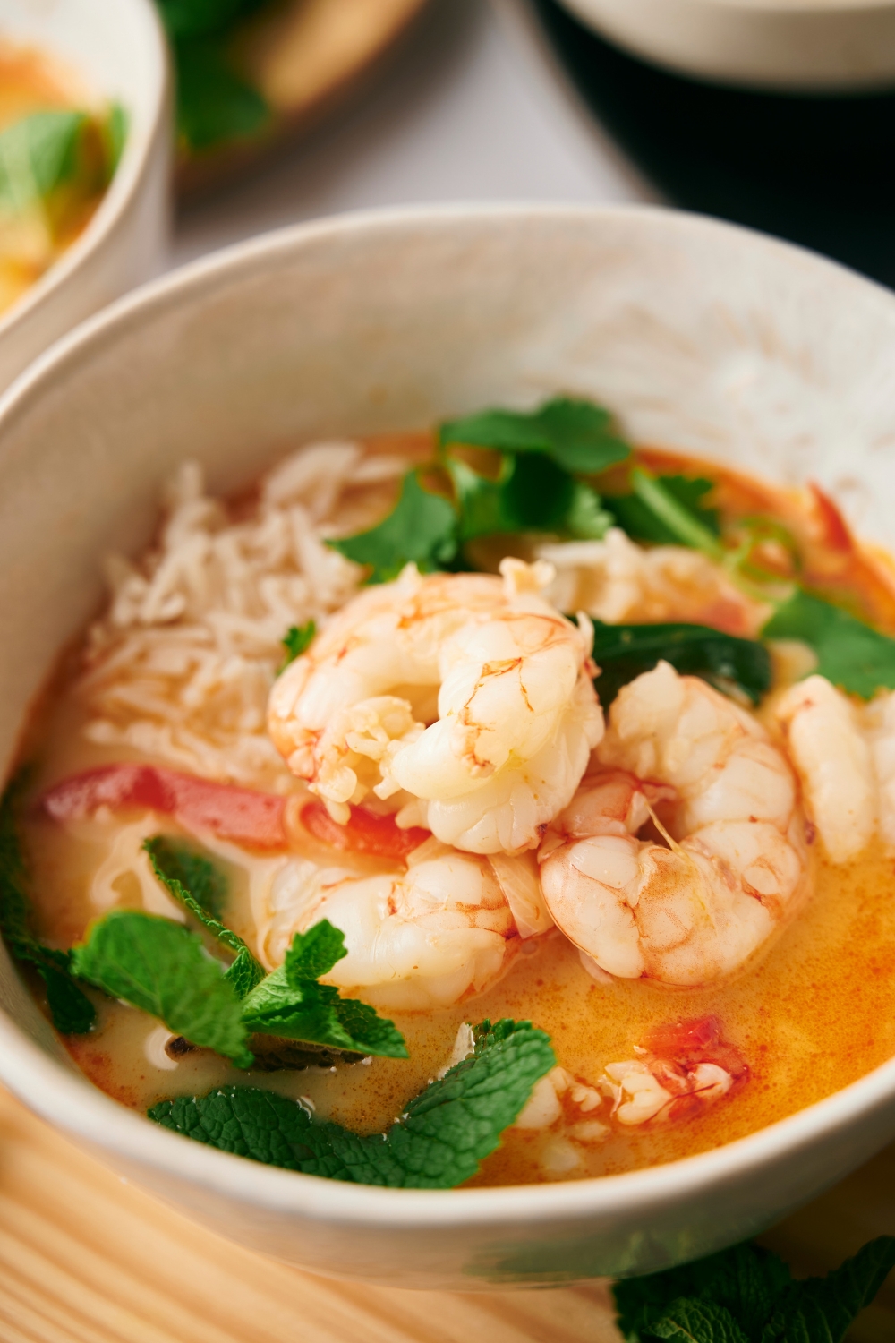 Shrimp in part of a white bowl that is filled with soup.