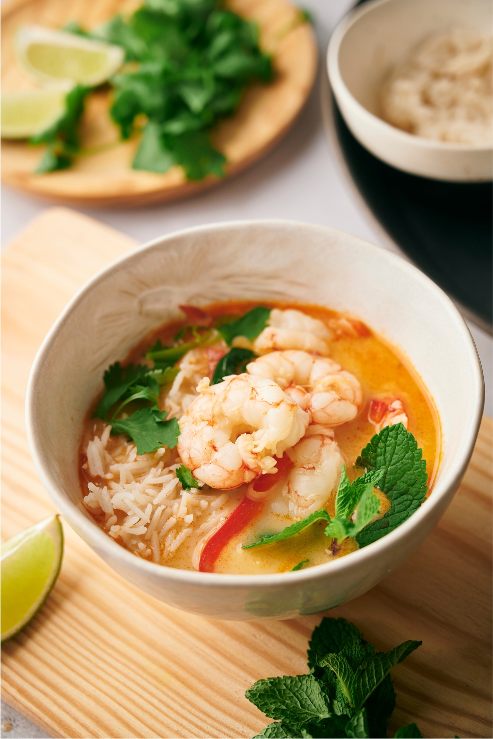 A white bowl that is filled with broth, rice, red bell pepper, and shrimp.