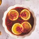 Cranberries and orange slices on top of holiday punch in a white punch bowl.