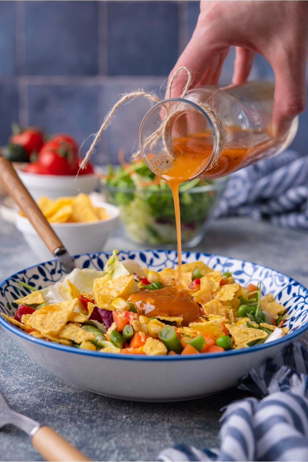 Hand drizzling vinaigrette over a salad of lettuce, tortilla chips, and assorted veggies.