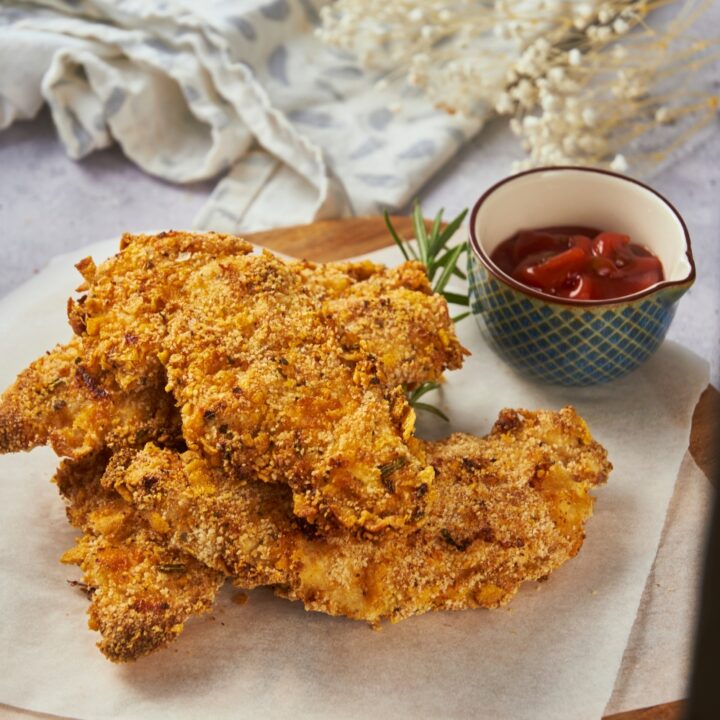 Zaxby's chicken fingers piled three-high on parchment paper on top of a wooden board with a bowl of ketchup.