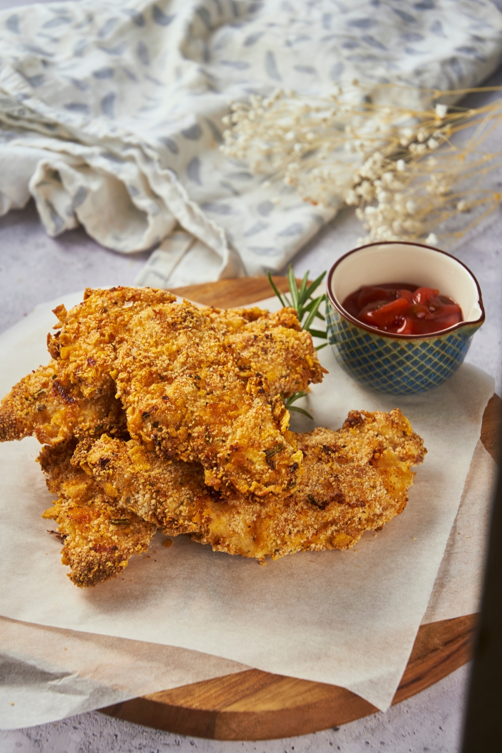 Zaxby's chicken fingers piled three-high on parchment paper on top of a wooden board with a bowl of ketchup.
