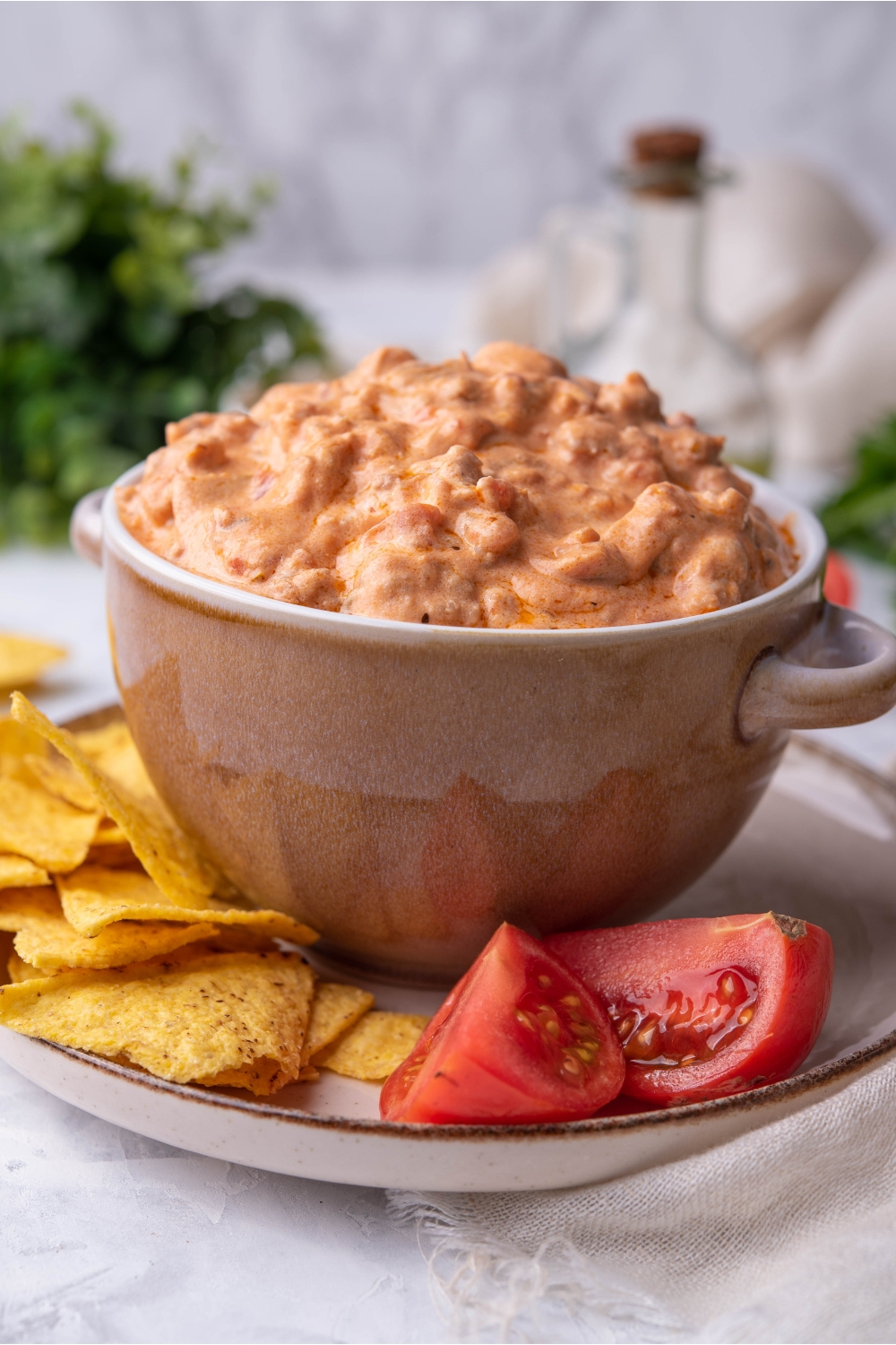 Cream cheese sausage dip in a serving bowl atop a plate of tortilla chips and tomato wedges.