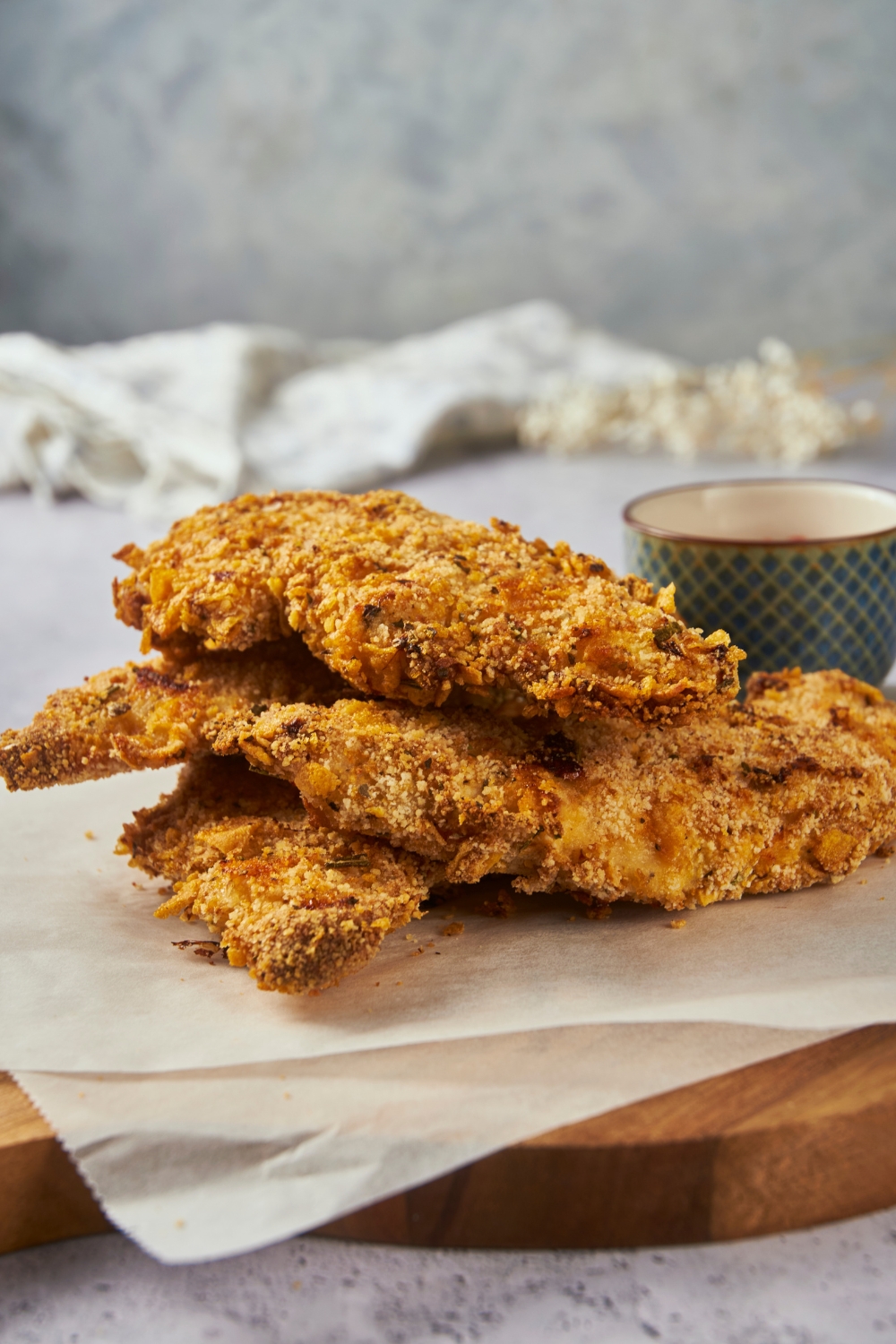 Zaxby's chicken fingers piled three-high on parchment paper on top of a wooden board with dipping sauce.