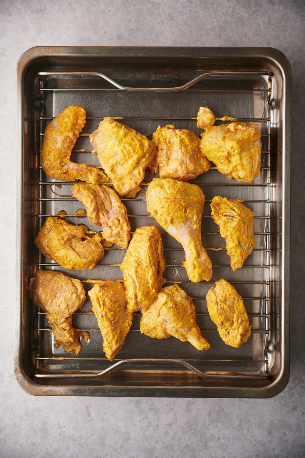 Unbaked tandoori chicken spread evenly on a grill pan that's on top of a roasting pan.