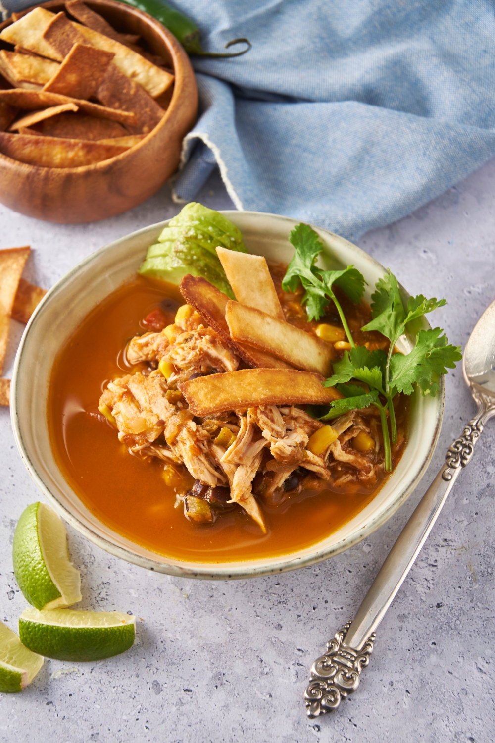 Chicken tortilla soup in an off-white bowl garnished with fresh cilantro, fried tortilla chips, and sliced avocado.
