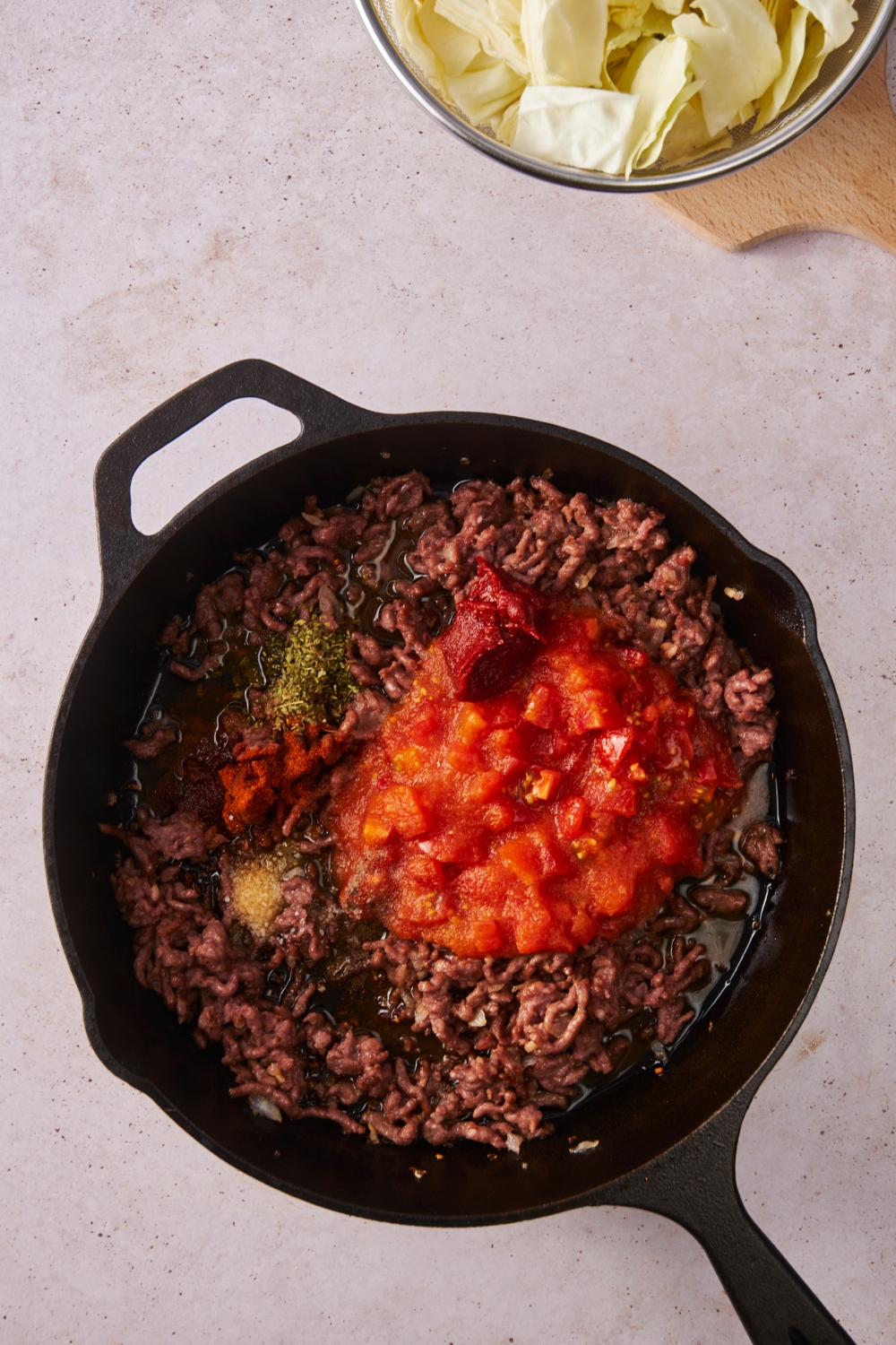 Black cast iron skillet filled with ground beef, crushed tomatoes, spices, and tomato paste.