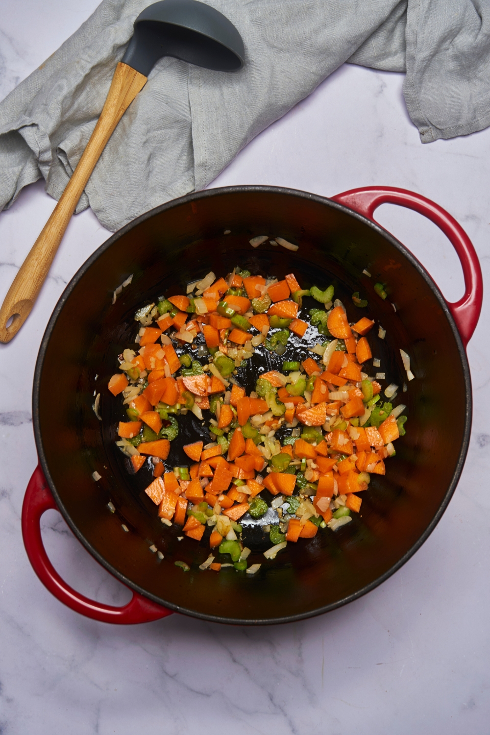 A red pot filled with diced carrot, celery, and onion sautéing in oil.