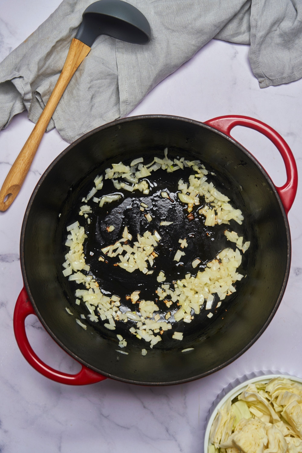 A large red pot with diced onion sautéing in oil.