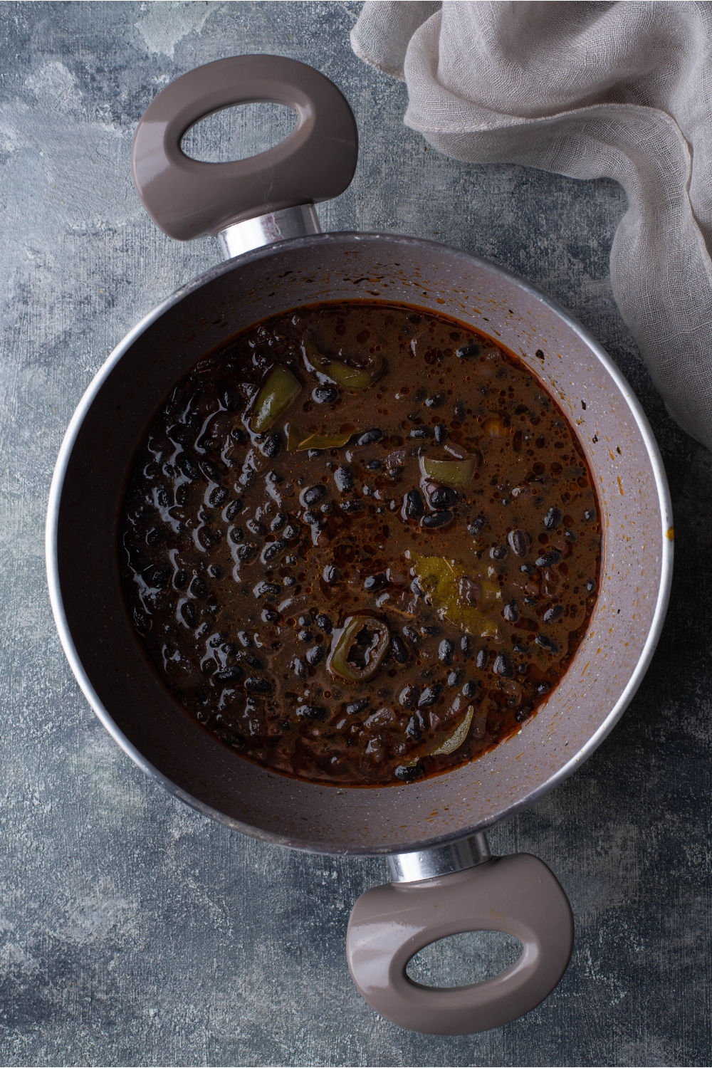 Sauce pot filled with black beans in a thickened liquid with sliced peppers.