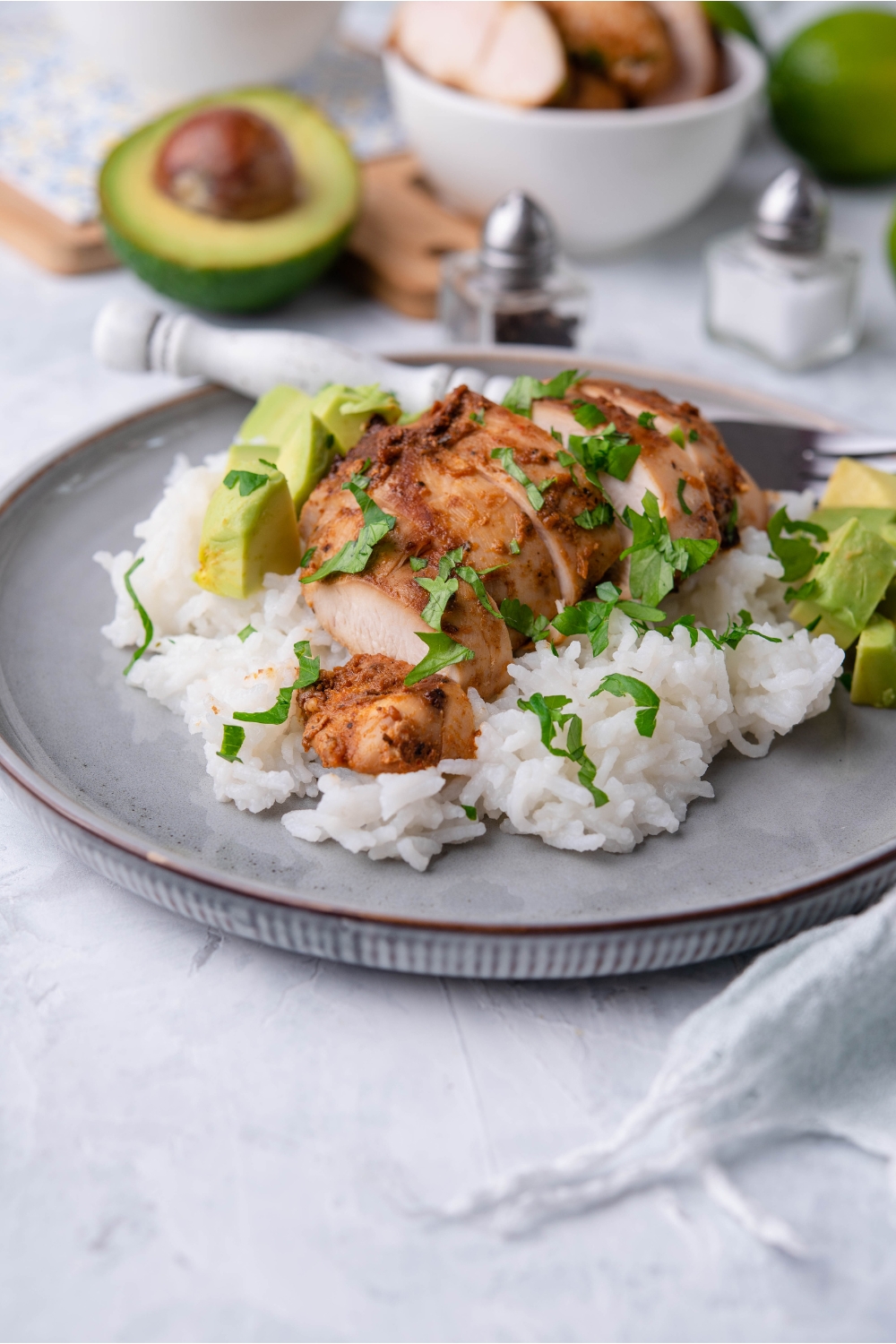 Chipotle chicken on a bed of white rice garnished with fresh herbs and diced avocado on a blue plate.