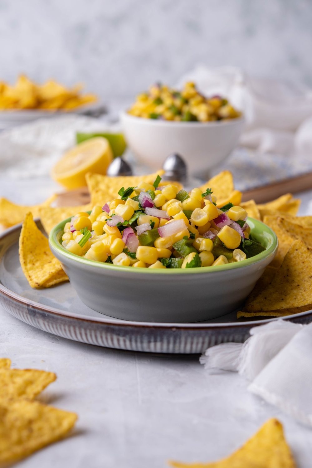 A small dip bowl with corn salsa and tortilla chips on the side of it.