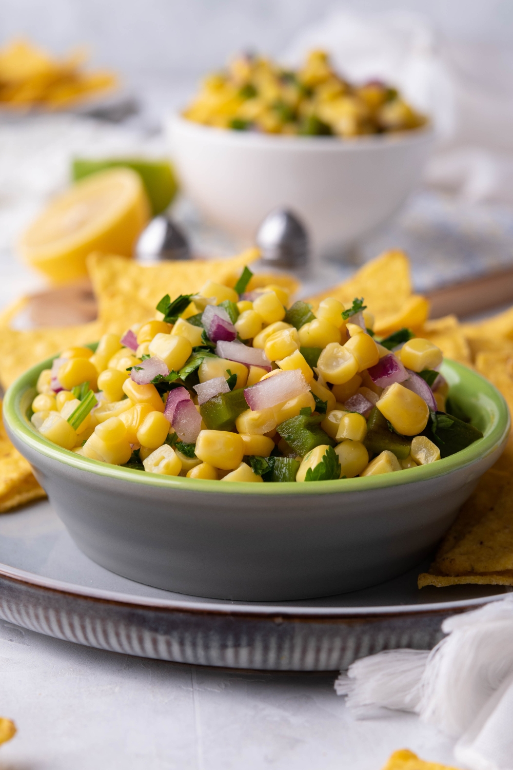 A small dip bowl with corn salsa and tortilla chips on the side of it.