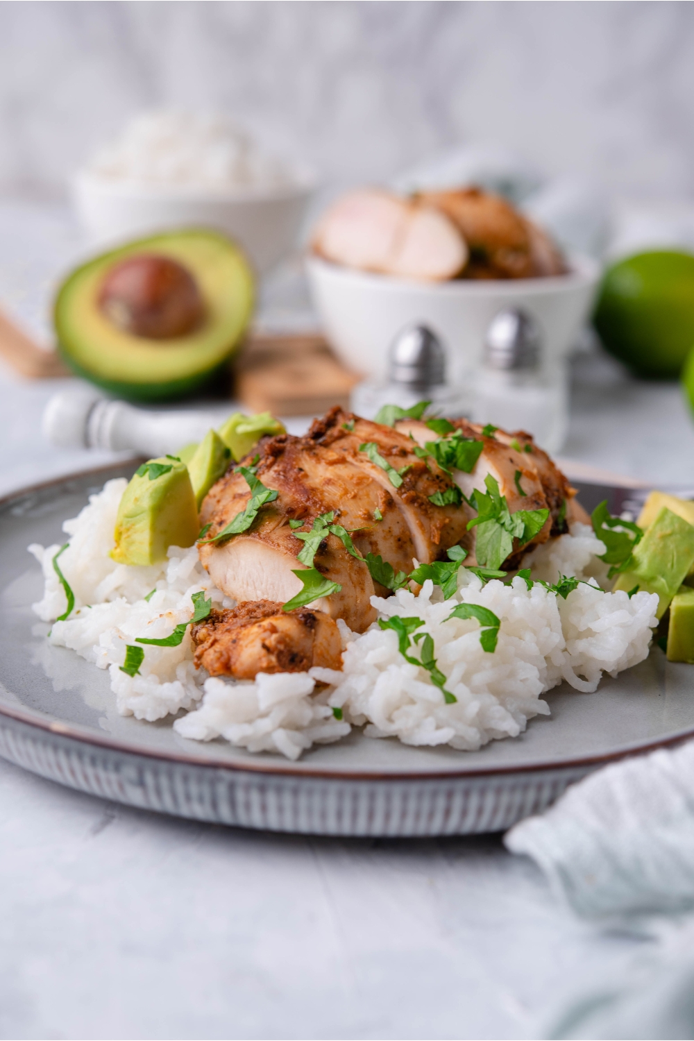Chipotle chicken on a bed of white rice garnished with fresh herbs and diced avocado on a blue plate.
