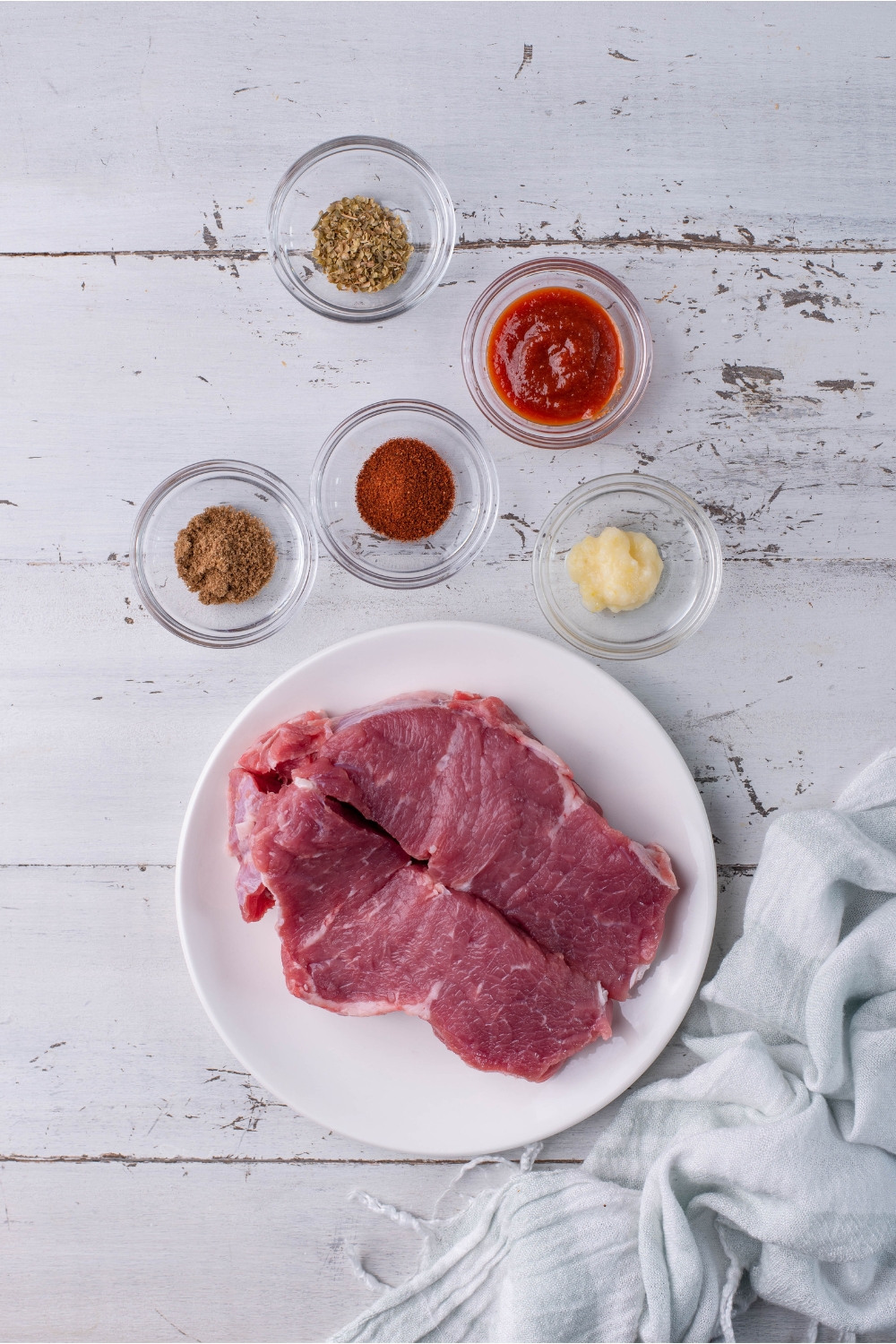 An assortment of ingredients including a plate of raw steak and bowls of spices.