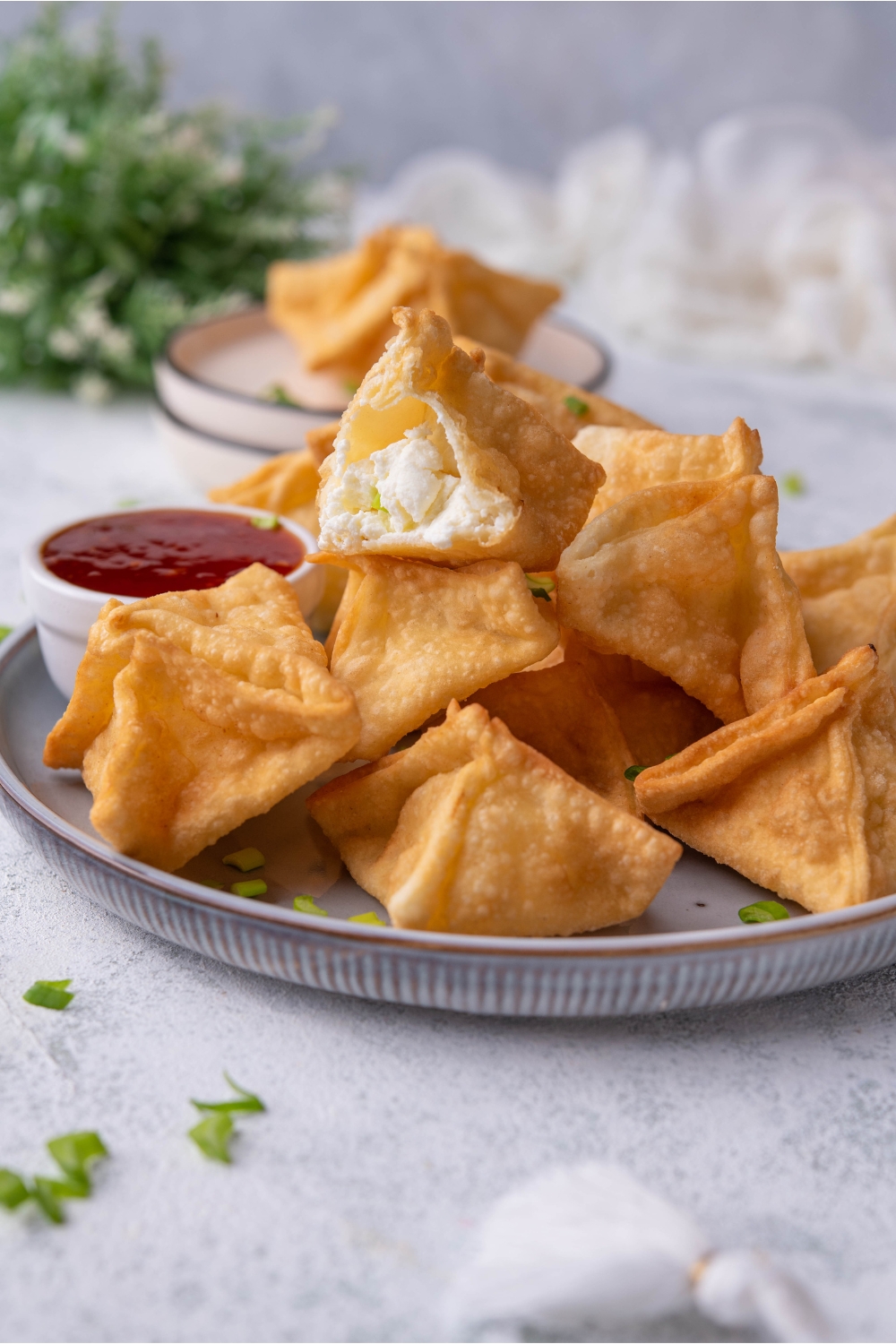 A pile of Panda Express cream cheese rangoon piled high on a plate with a serving of dipping sauce. A bite has been taken out of one of the rangoon.
