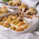 Cowboy casserole in a white baking dish with a serving being scooped out.