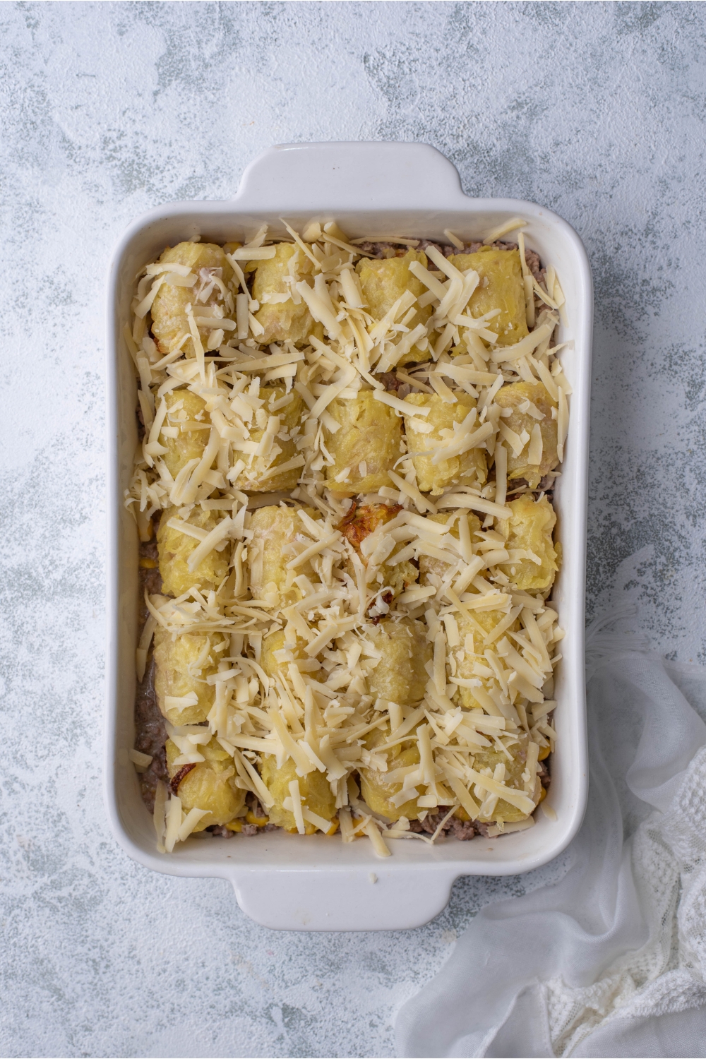 White baking dish with unbaked cowboy casserole covered in shredded cheese.