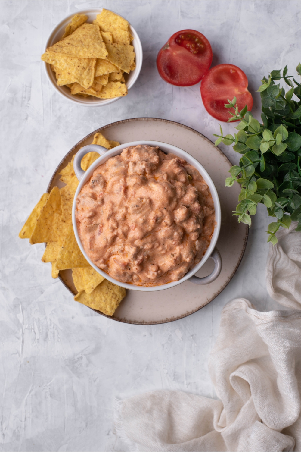 Cream cheese sausage dip in a serving bowl atop a plate of tortilla chips, surrounded by sliced tomatoes and a second bowl of tortilla chips.