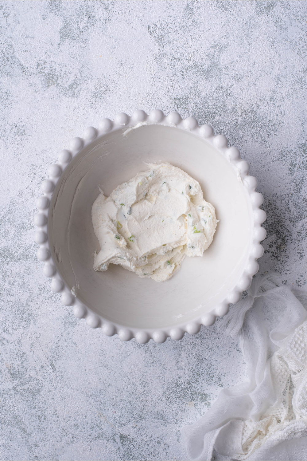 A decorative white bowl filled with cream cheese and green onion that have been mixed together.