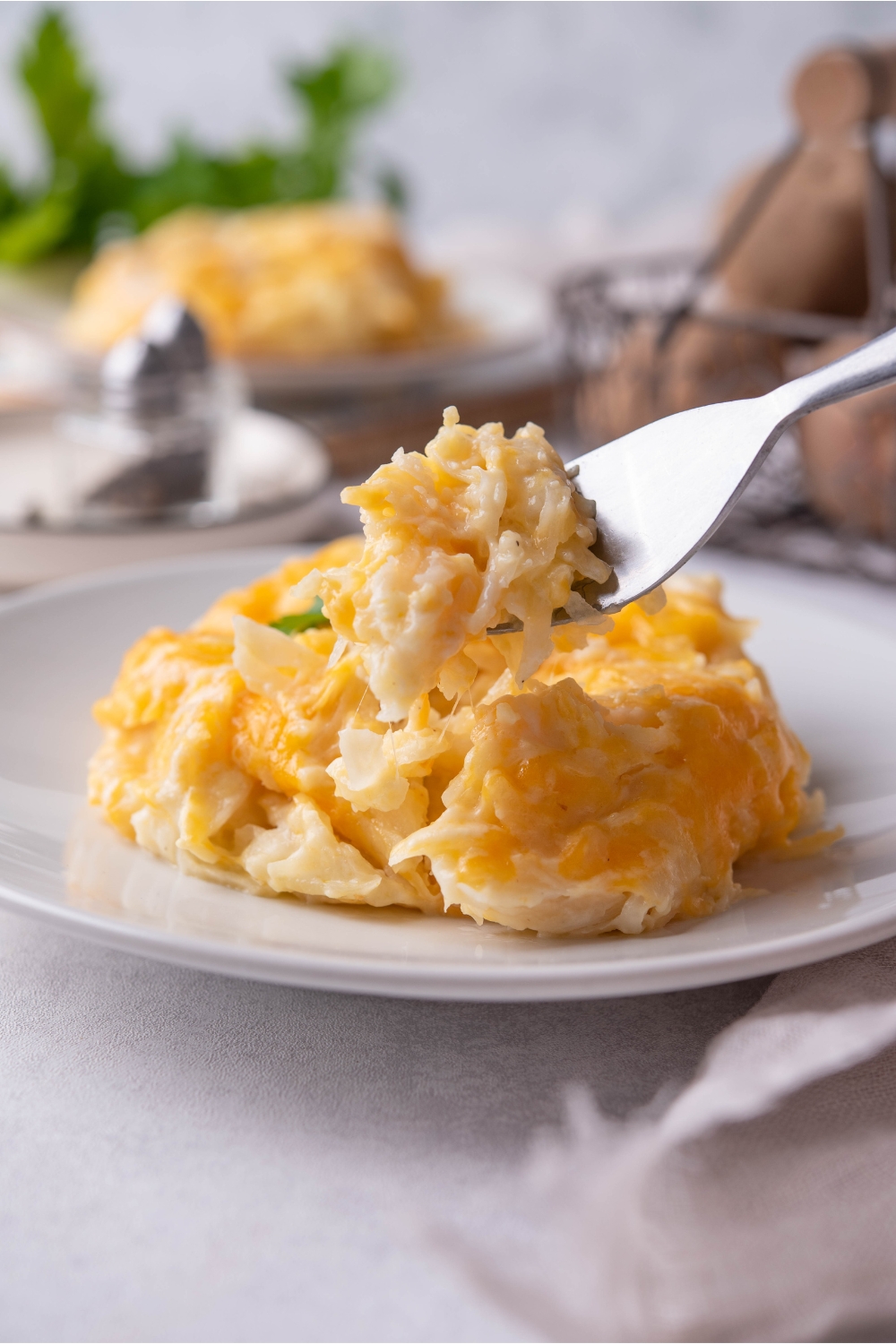 A serving of crockpot cheesy potatoes on a white plate with a fork holding a bite of cheesy potatoes.