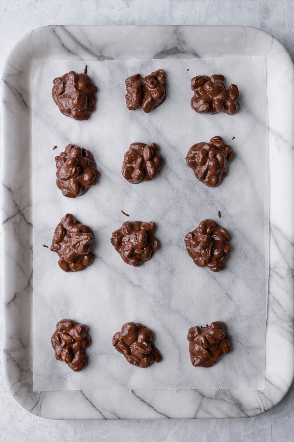 Chocolate peanut clusters lined on a marble serving tray on parchment paper.