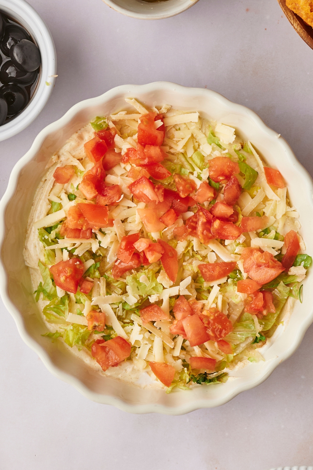 A serving bowl with creamy taco dip base, shredded lettuce, and diced tomatoes on it.