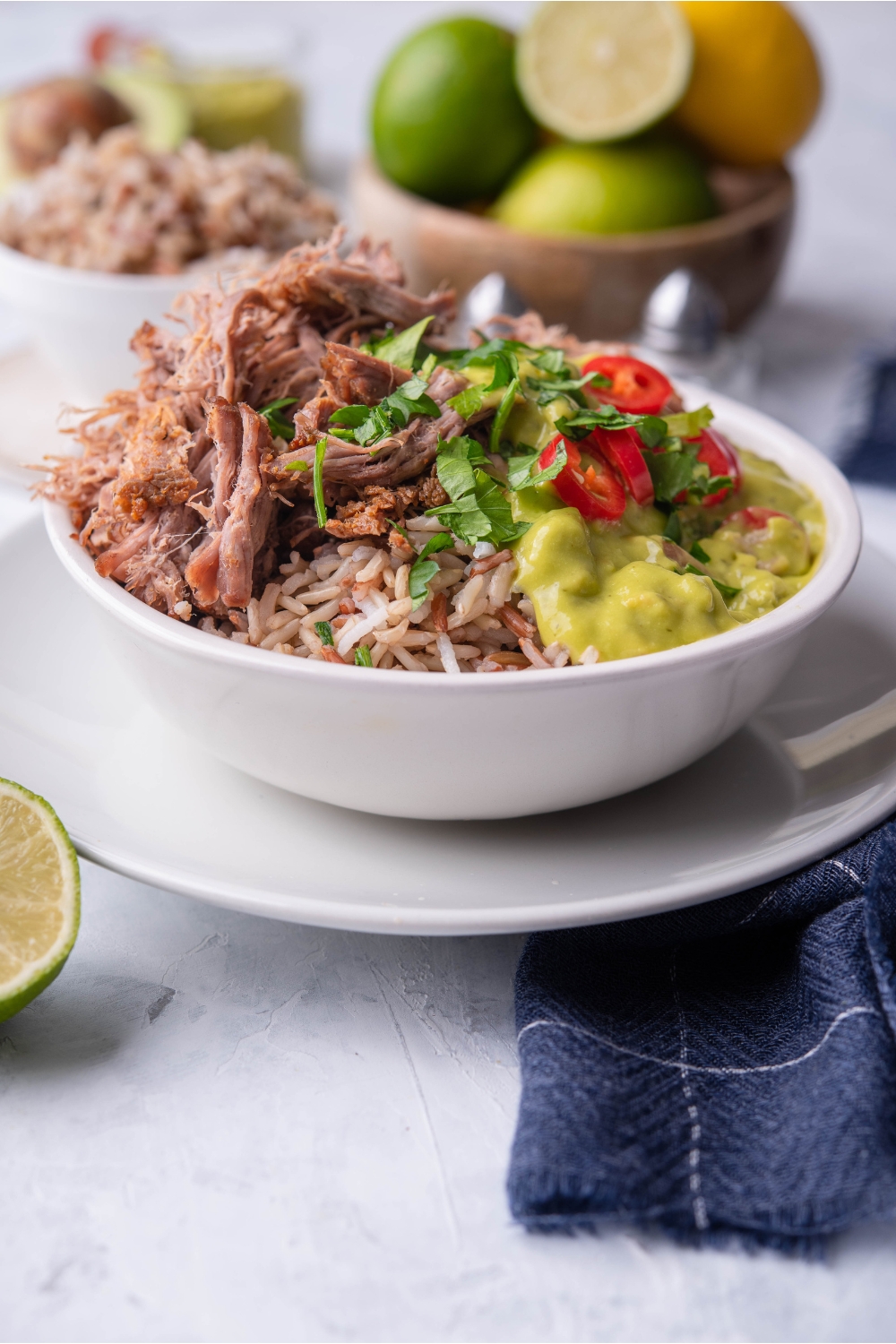 Shredded barbacoa in a bowl with brown rice, sliced peppers, guacamole, and fresh herbs.