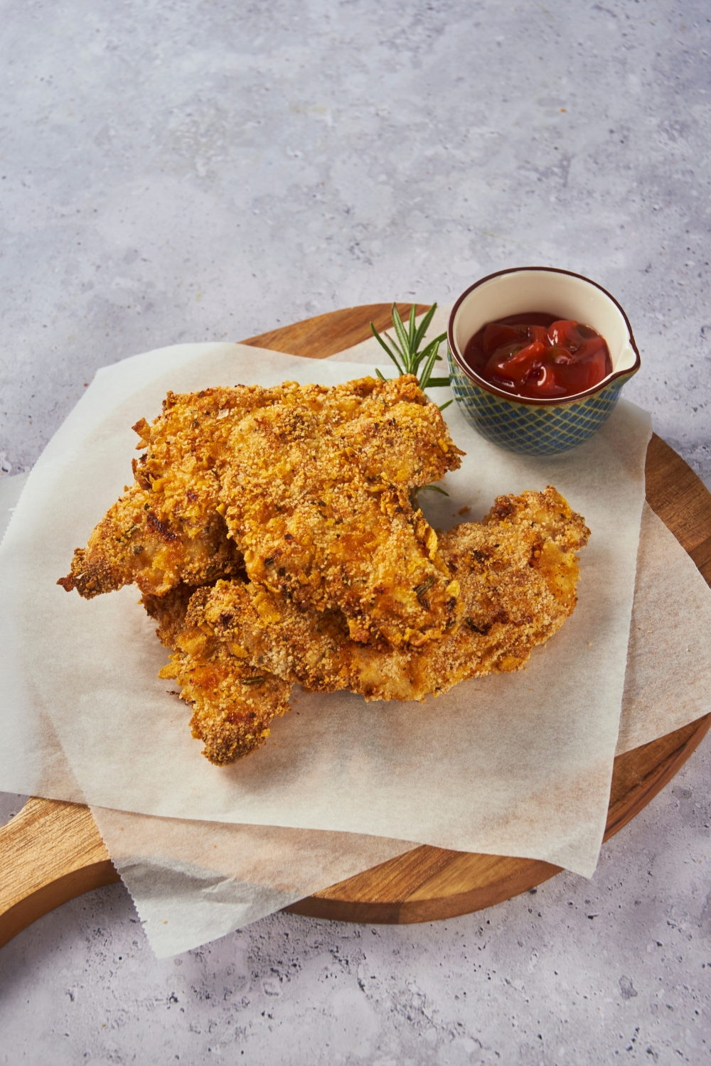 Zaxby's chicken fingers piled three-high on parchment paper on top of a wooden board with dipping sauce.