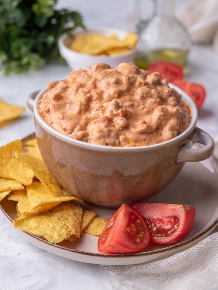 Cream cheese sausage dip in a serving bowl atop a plate of tortilla chips and tomato wedges.