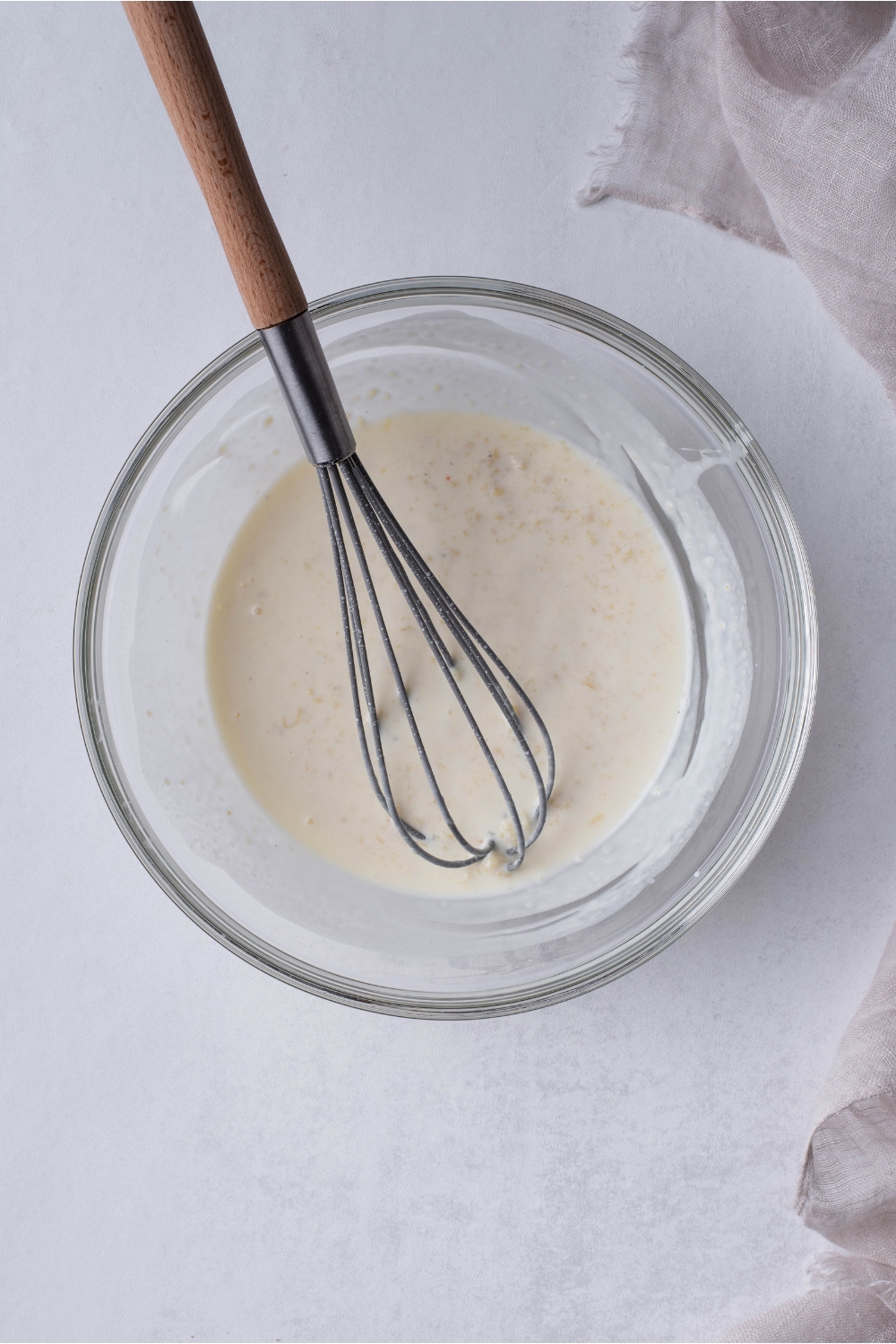 A clear bowl with a soup mixture that has been mixed with a whisk that is still in the bowl.