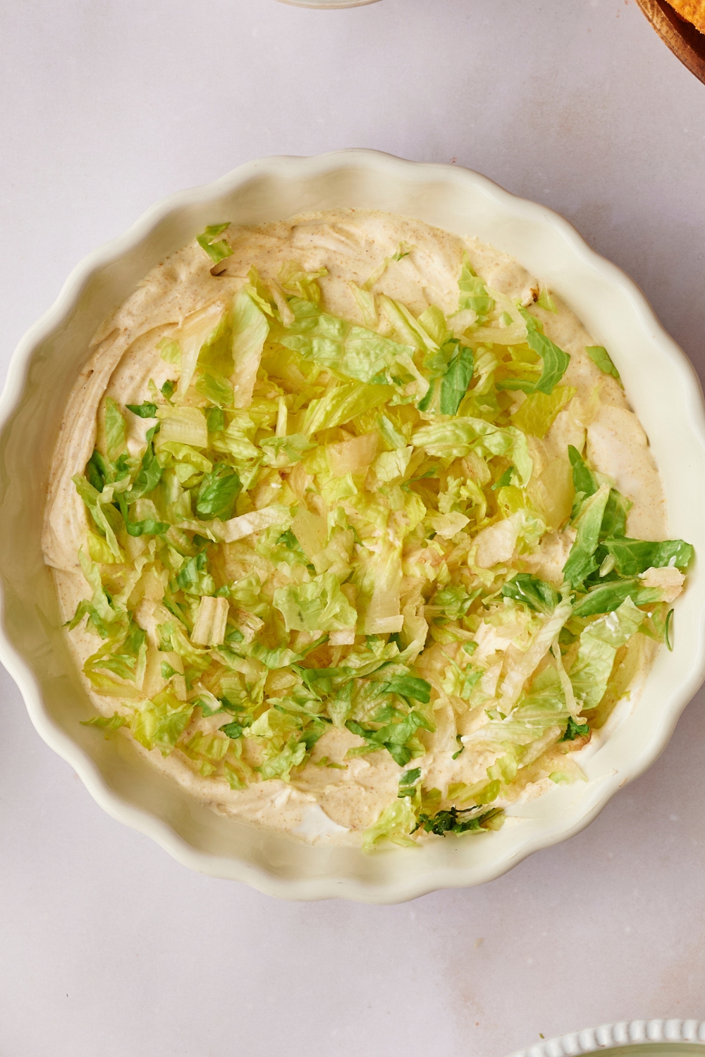 A serving bowl with creamy taco dip base and shredded lettuce on it.