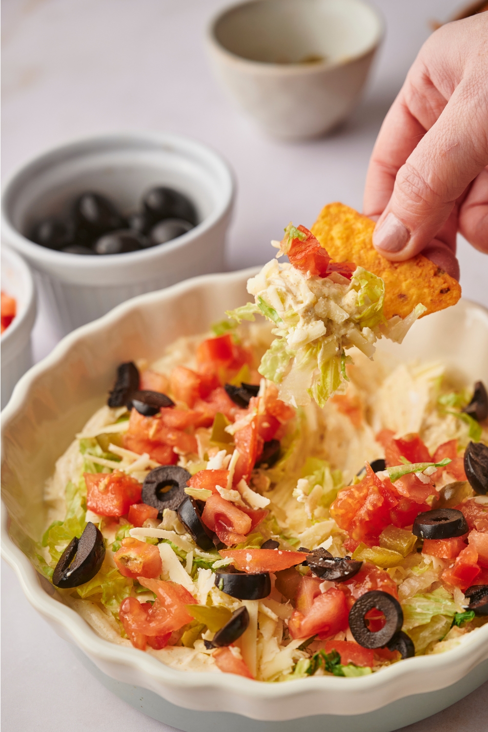 A servings dish with a cheesy tortilla chip being dipped into taco dip.