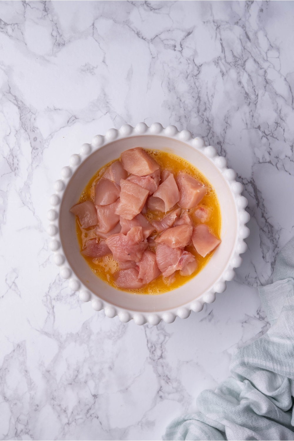 A white bowl filled with raw chicken pieces in a mixture of beaten eggs.