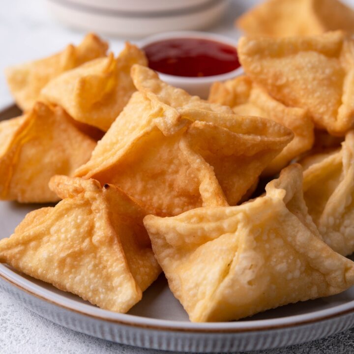 Close up of Panda Express cream cheese rangoon piled on a grey plate with a dipping sauce on the plate.