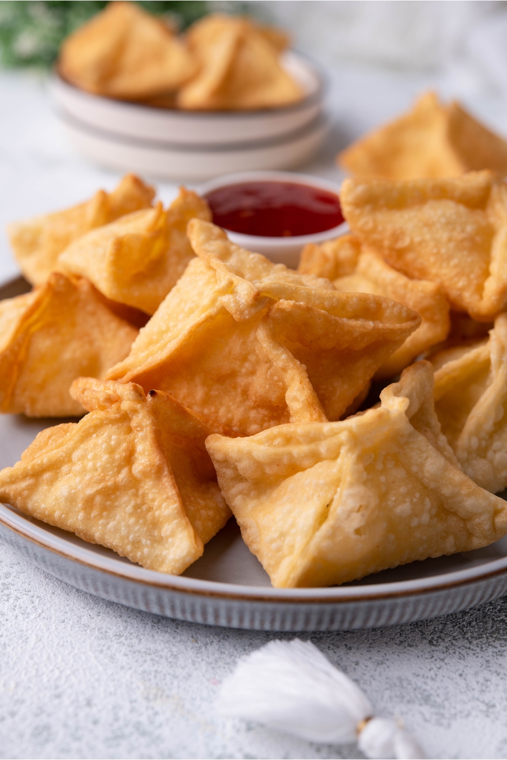 Close up of Panda Express cream cheese rangoon piled on a grey plate with a dipping sauce on the plate.