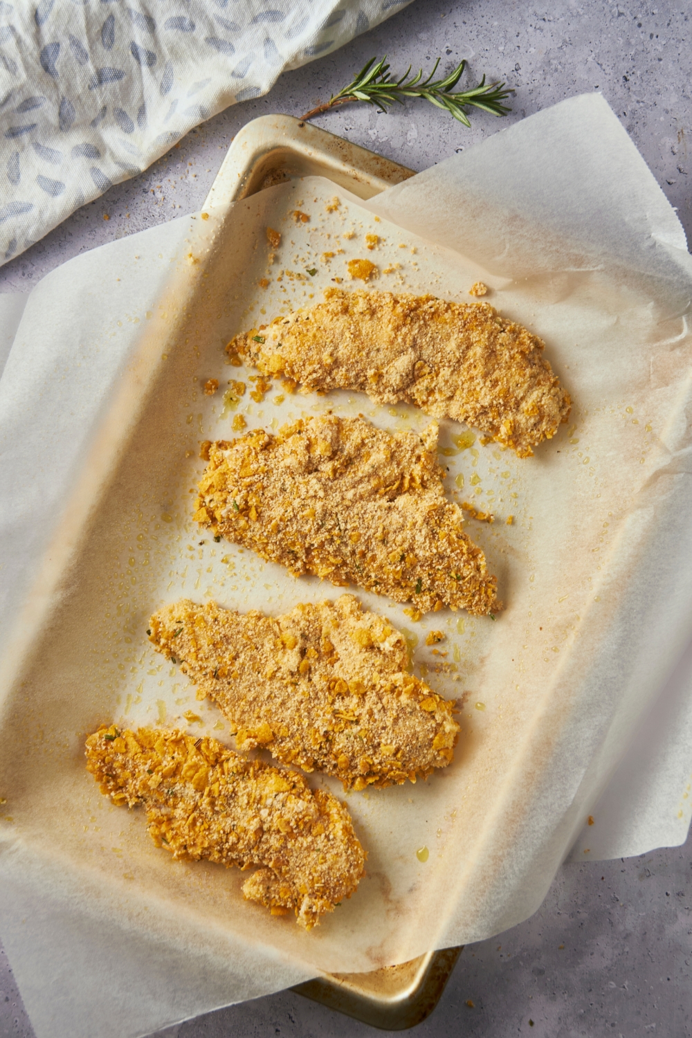 Four pieces of breaded chicken tenders on a baking sheet lined with parchment paper.
