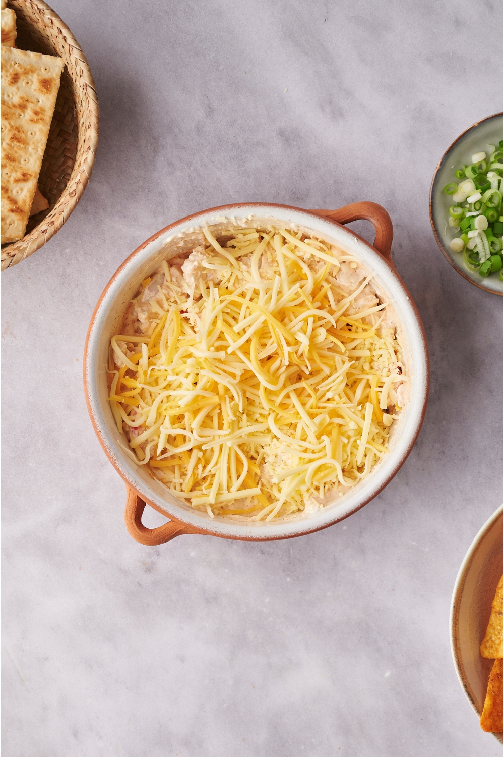 Overview of unbaked crab dip covered in shredded cheese in a white and brown baking dish.