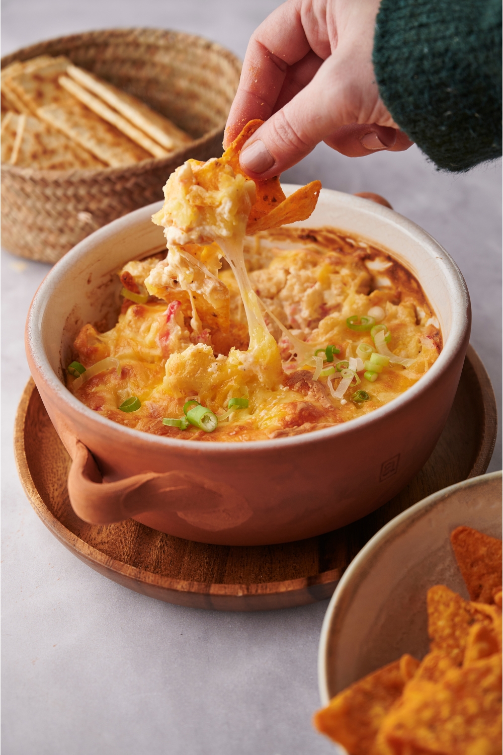 Hand scooping cheesy crab dip out of a baking dish with a tortilla chip.