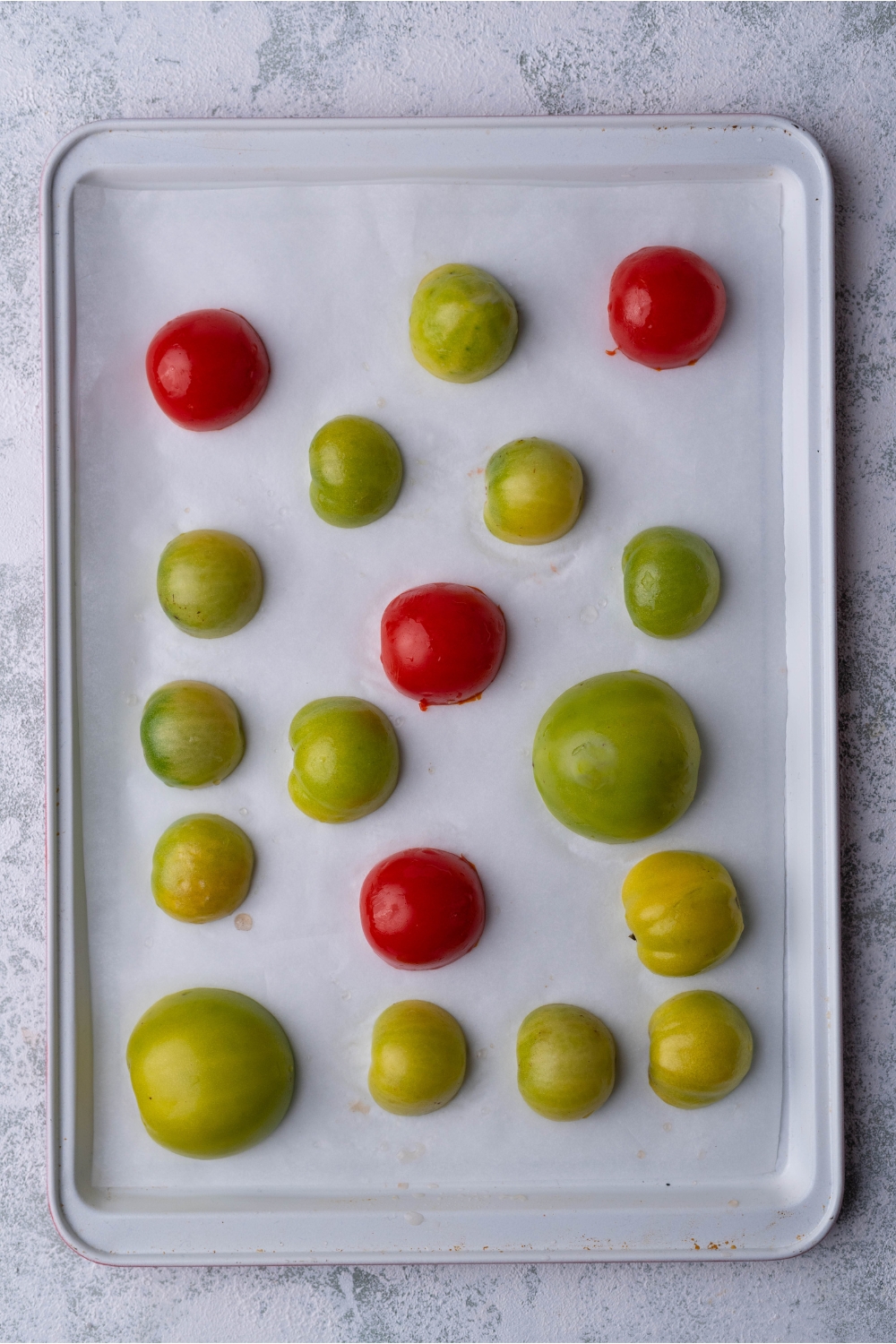 Halved tomatillos, green tomatoes, and cherry tomatoes face-down on a baking sheet lined with parchment paper.