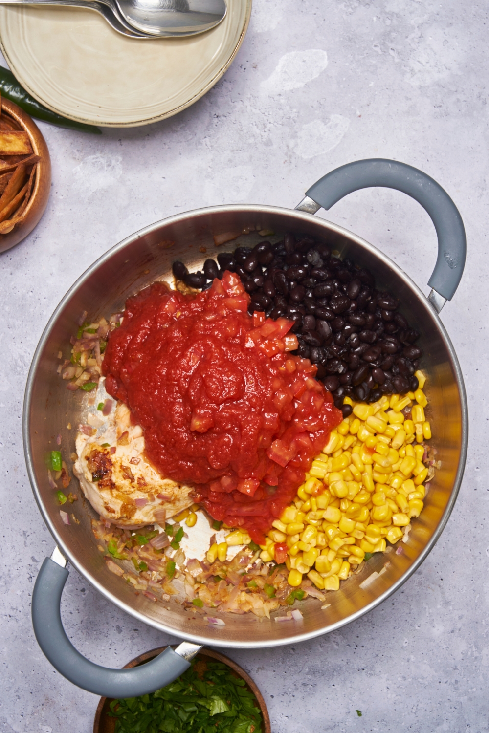 A pot filled with diced peppers, onion, a whole chicken breast, black beans, crushed tomatoes, and corn.