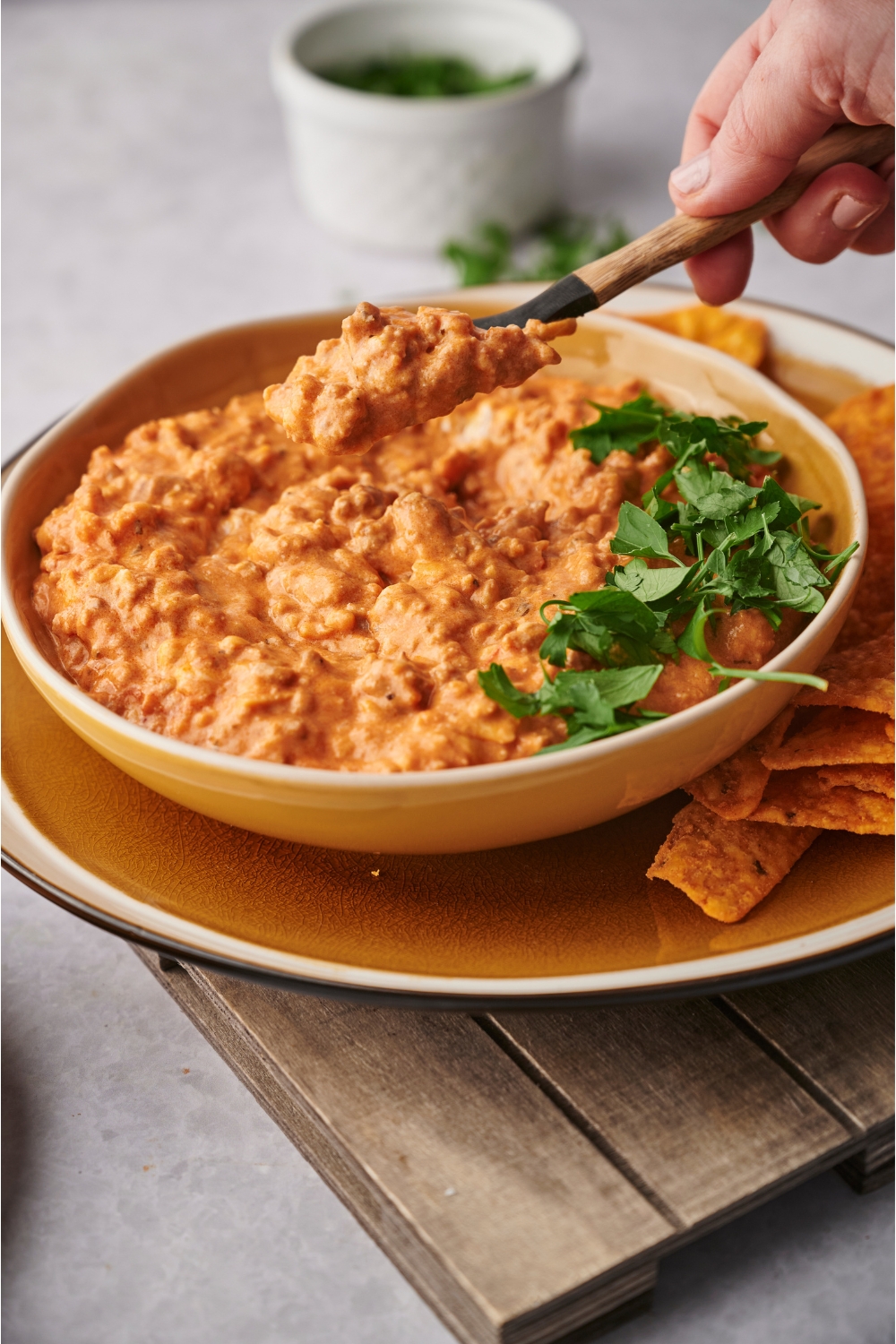 Hand scooping a spoonful of chili cheese dip out of the serving bowl filled with dip.