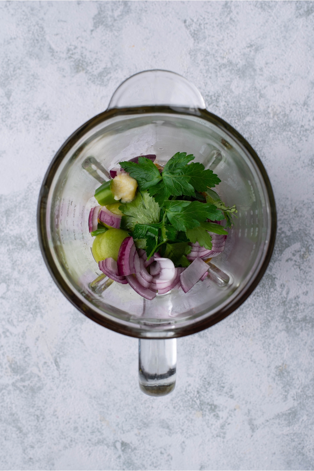 A blender filled with cilantro, garlic paste, red onion, and tomatillos.