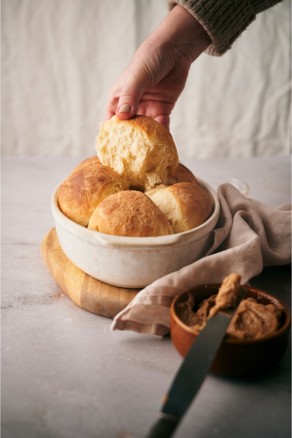 Hand grabbing a dinner roll from a white baking dish.