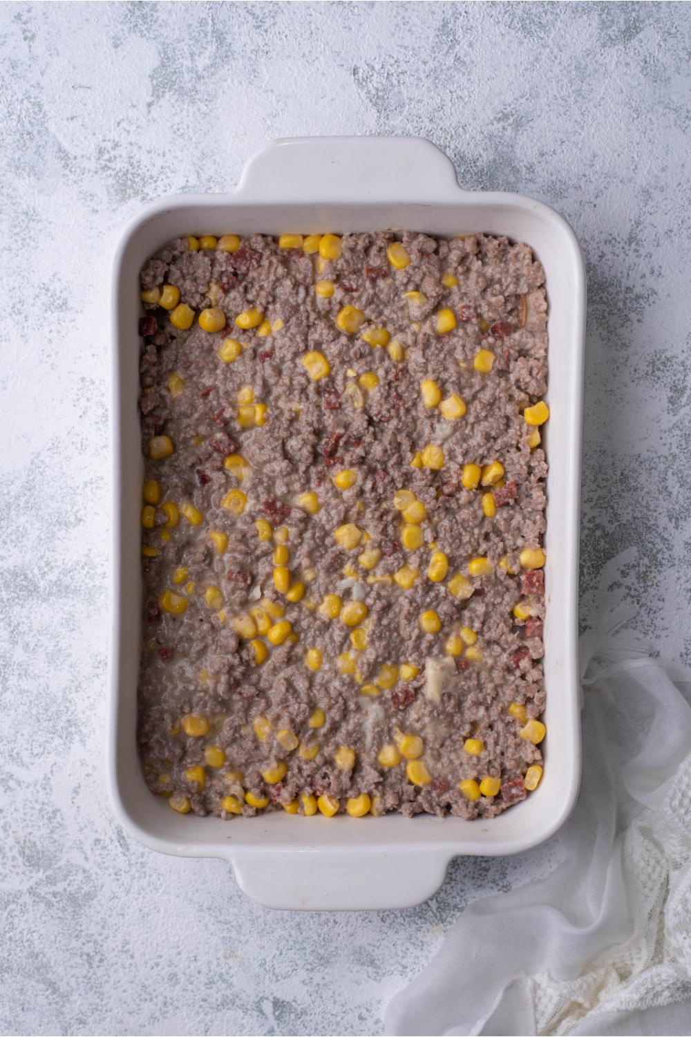 White baking dish layered with cooked ground beef and corn in a creamy sauce.