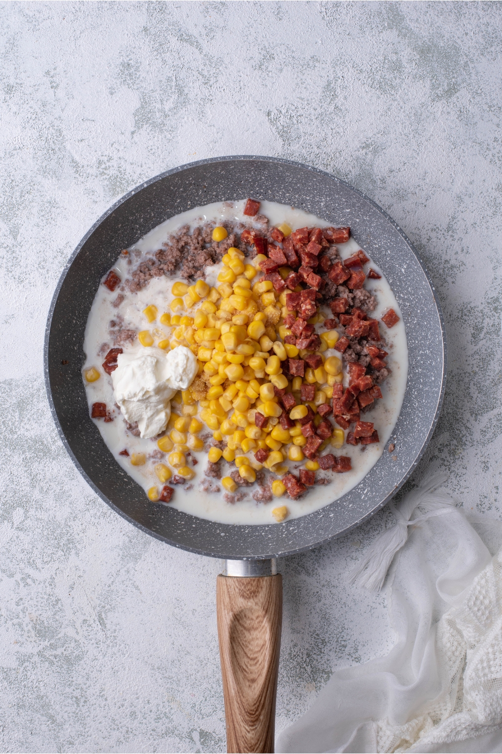 Skillet filled with cooked ground beef, diced chorizo, corn, and sour cream in a creamy soup mixture.