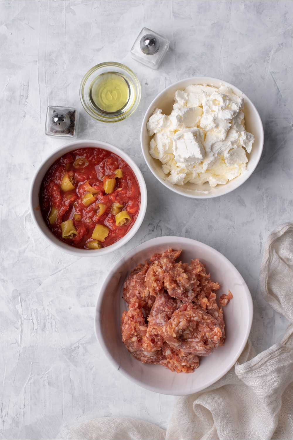 An assortment of ingredients including bowls of cream cheese, crushed tomatoes, and raw ground beef.