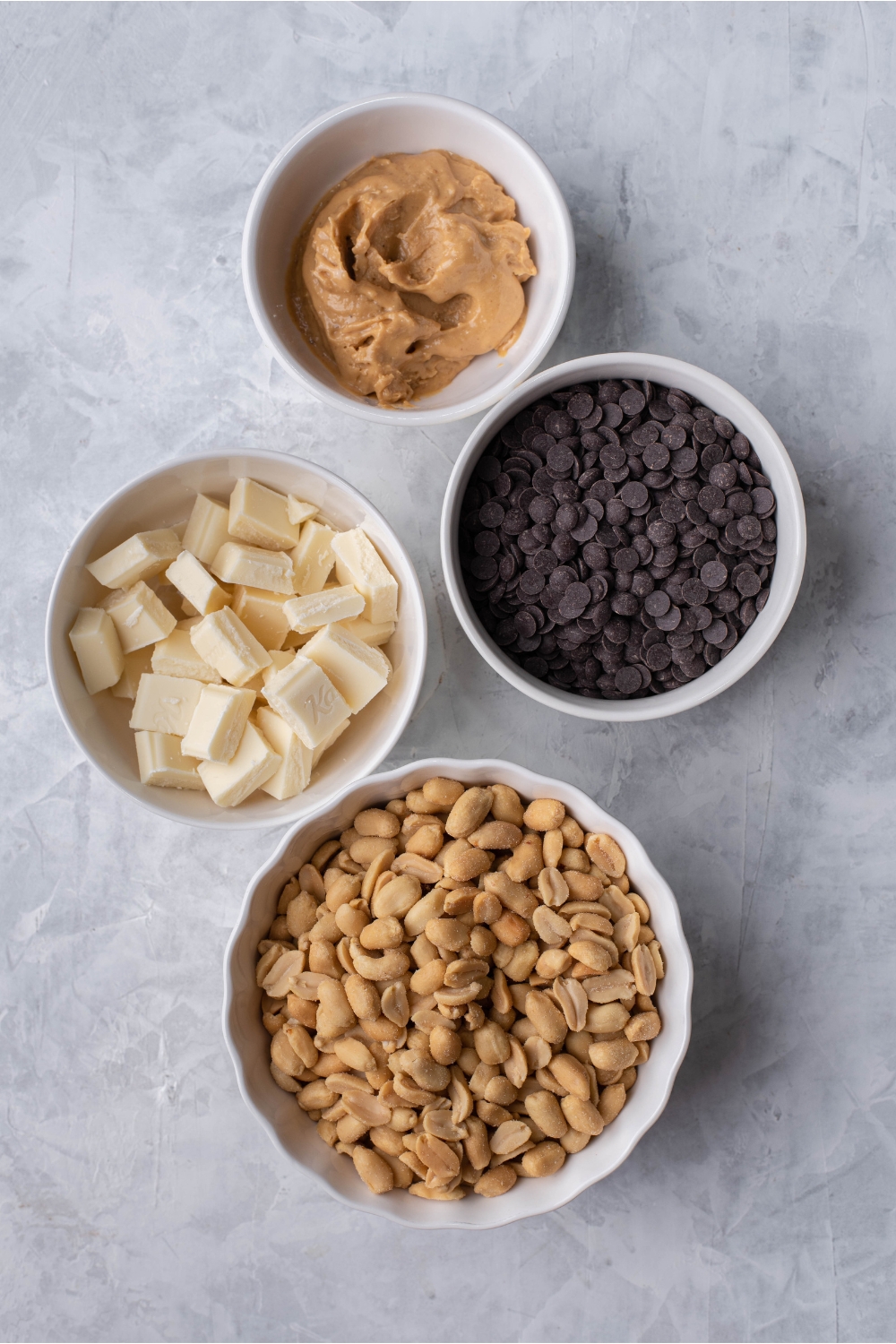 An assortment of ingredients including bowls of chocolate chips, peanuts, white chocolate, and peanut butter.